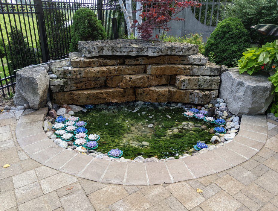 A stone fountain surrounded by rocks and grass.